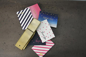 Stripe, dot and ombre thank you cards in large gold clip scattered on concrete surface