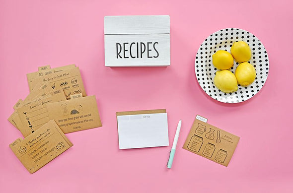 White vintage farmhouse recipe box alongside kraft paper recipe card dividers on pink backdrop
